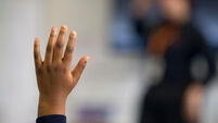 A young black child puts his hand up when asked a question in a school classroom in Wales, UK.