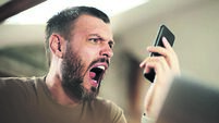 Angry man yelling while using cell phone while working at home.