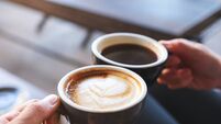 Closeup image of a man and a woman clinking white coffee mugs in cafe