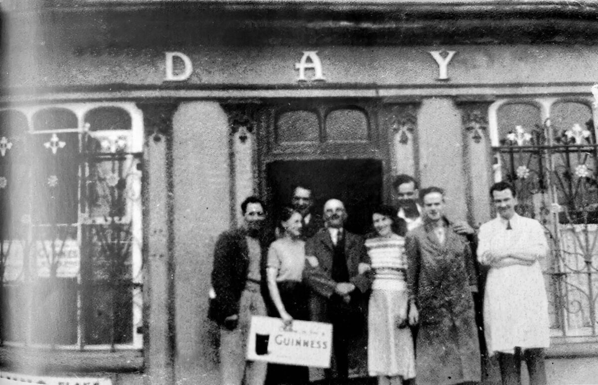 A group of people outside Day’s pub in Whitegate with proprietor William Day centre with moustache. Kevin Day is in the white coat, his son, a butcher, with Day employee Davy Ryan beside him. Picture supplied by Micheál Kenefick A group of people outside Day’s pub in Whitegate with proprietor William Day centre with moustache. Kevin Day is in the white coat, his son, a butcher, with Day employee Davy Ryan beside him. Picture supplied by Micheál Kenefick