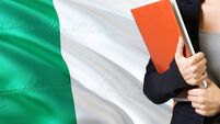 Learning Irish language concept. Young woman standing with the Ireland flag in the background. Teacher holding books, orange bla