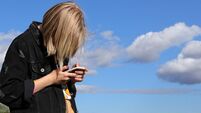 Teen girl playing online games by a smartphone on blue sky background. The concept of teenage addiction to a mobile phone and so