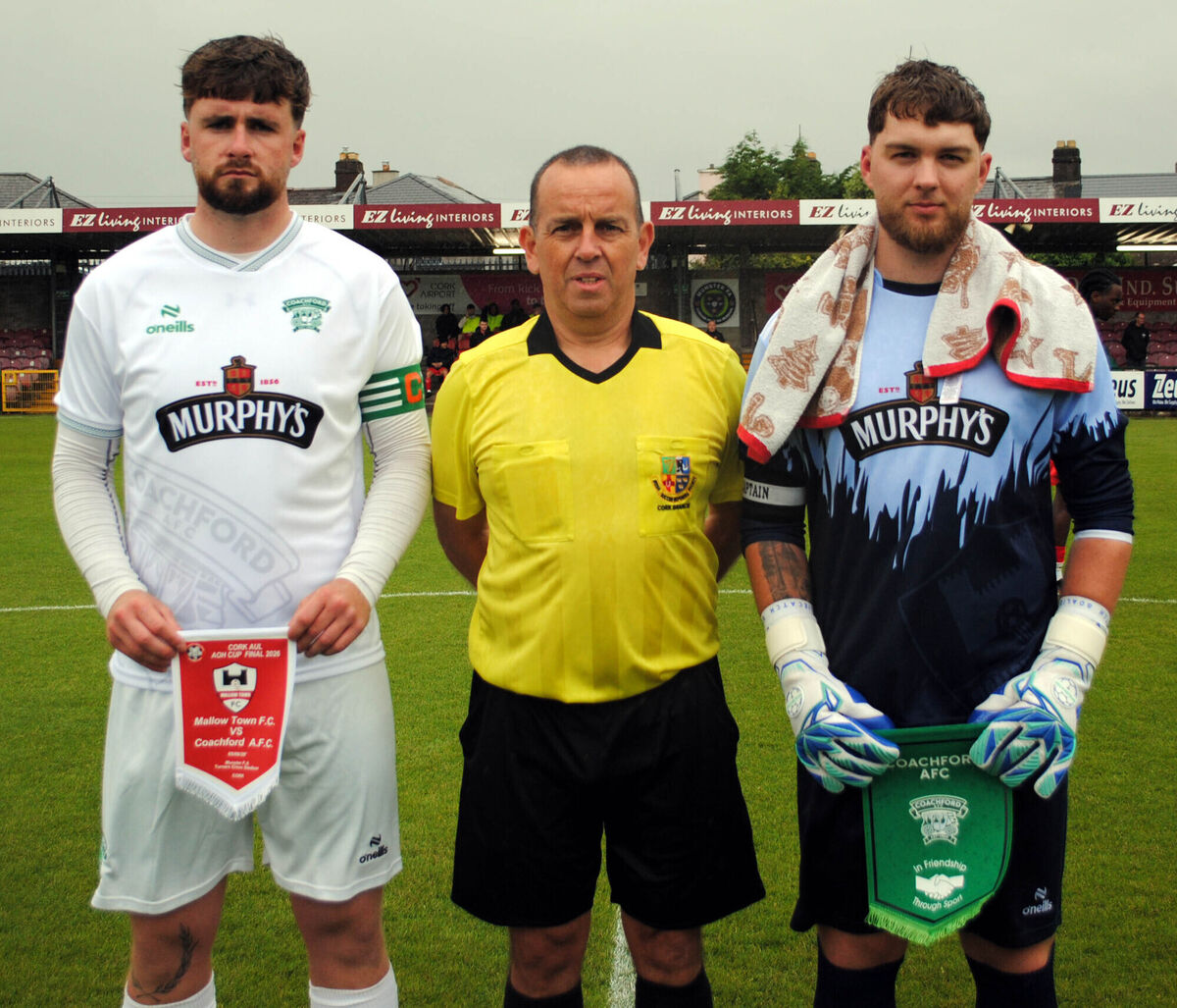 Coachford A's Mark Murphy (left) and Mallow Town's Artur Osinski exchanged pennants, with referee Stephen Moore. Picture: Barry Peelo.