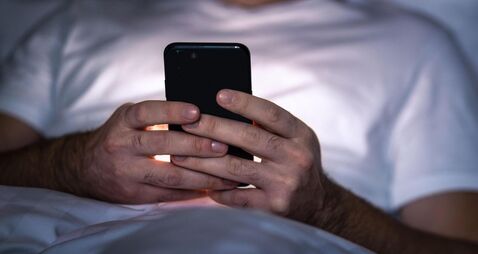 Phone in bed at night. Man with smartphone before sleeping. Secret texting, cheating or working late. Happy guy browsing online
