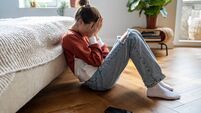 Unhappy teen girl covering face with hands crying while sitting on floor with mobile phone nearby