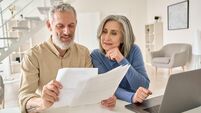 Middle aged couple reading paper bills calculating pension using laptop at home.