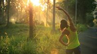Young female runner warming up before running at morning forest trail