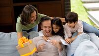 Happy father opening his present for Father's Day while celebrating with his family