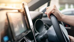 iStock-1044224036.jpg Male driver hand holding on steering wheel using smartphone for GPS navigation. Mobile phone mounting with magnet on the car con