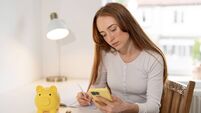 Young woman managing finances at home with phone and piggy bank