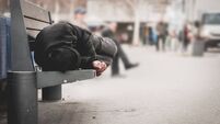 Poor homeless man or refugee sleeping on the wooden bench on the urban street in the city, social documentary concept, selective