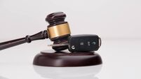 Close-up Of Gavel And Car Key On Sounding Block Against Grey