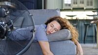 Young woman lying in front of the electric fan at home, overwhelmed by the heat