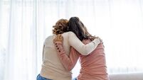Rear view of mother and daughter embracing sitting on bed