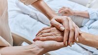 Relative holding trembling hand of senior woman with Parkinson's disease lying in hospital bed at medical ward. Diagnosis and tr
