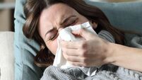 Ill woman suffering flu symptoms blowing on tissue lying on a couch at home
