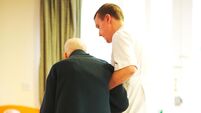 Elderly care home patient is helped by male nurse in the common space of the dementia home