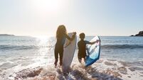 Rear View Of Two Children Wearing Wetsuits Running Into Sea With Bodyboards On Beach Vacation