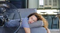 Young woman lying in front of the electric fan at home, overwhelmed by the heat