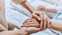 Relative holding trembling hand of senior woman with Parkinson's disease lying in hospital bed at medical ward. Diagnosis and tr