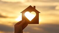 Woman hand holds wooden house in the form of heart against the sun