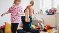 Stressed out mother sitting on floor while children running around her.