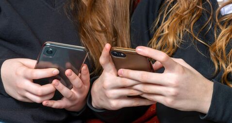 teenage school girls being cyber bullies  or just catching up on social media both on there phones, hand level  copy space above