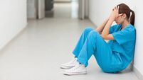 Nurse sitting in a corridor while holding her head