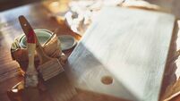 Brushes lie next to the painted wooden board on the sunny table