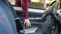 Hooded thief stealing a computer laptop from a parked car