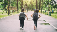 Two pupils of primary school run go to shool. Two girl with bags behind the back. Warm day of fall. Back to school. Little first