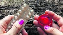 young woman holding a birth control pills and a condom
