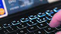 A hand typing on a keyboard with a computer screen and credit cards in the background. Concept: fraud using stolen credit cards