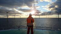 Offshore manual worker standing on helipad with wind-turbines behind him in sunset