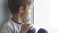 Sad lonely child sitting alone on the window at home