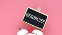 Alarm clock and word menopause on a pink background.