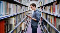 student reading book between the shelves in the library