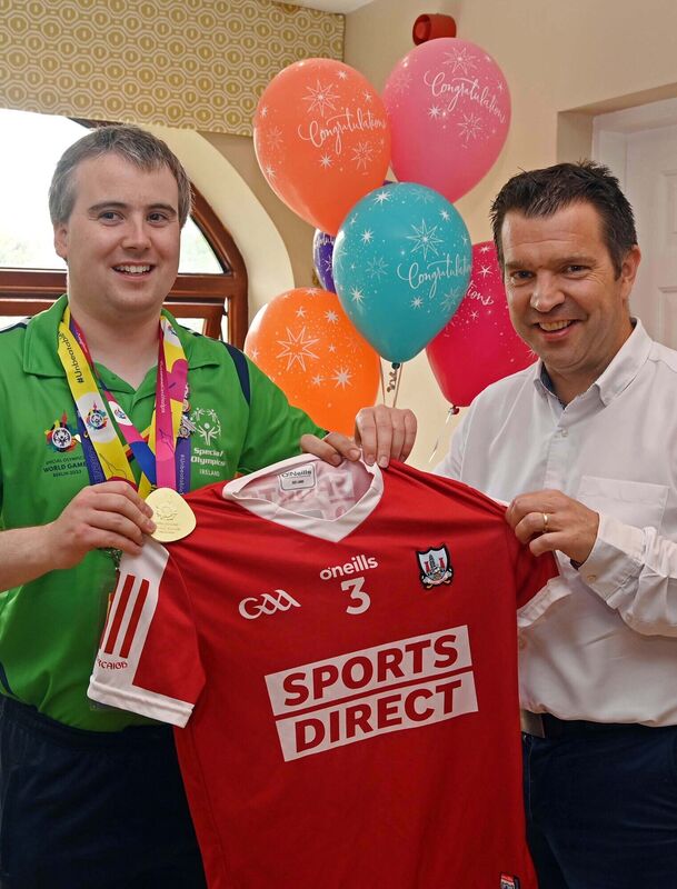 Colm Monahan, a member of the staff at Chapel Gate Café, Ballincollig, run by the Brothers of Charity, during a celebration in his honour at the café on his return with a men's singles gold medal for badminton at the Special Olympics World Games, being presented with a jersey from the Cork minor football team by the team manager Ray O'Mahony. Colm Monahan, a member of the staff at Chapel Gate Café, Ballincollig, run by the Brothers of Charity, during a celebration in his honour at the café on his return with a men's singles gold medal for badminton at the Special Olympics World Games, being presented with a jersey from the Cork minor football team by the team manager Ray O'Mahony.