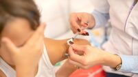 Shot of human hands making an injection with a syringe to a little girl who is afraid to look. Selective focus