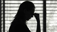 Tired woman standing next to bedroom window.