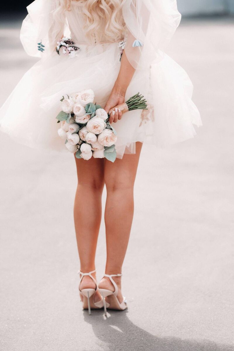  A bride with a short wedding dress holds a bouquet behind her back.