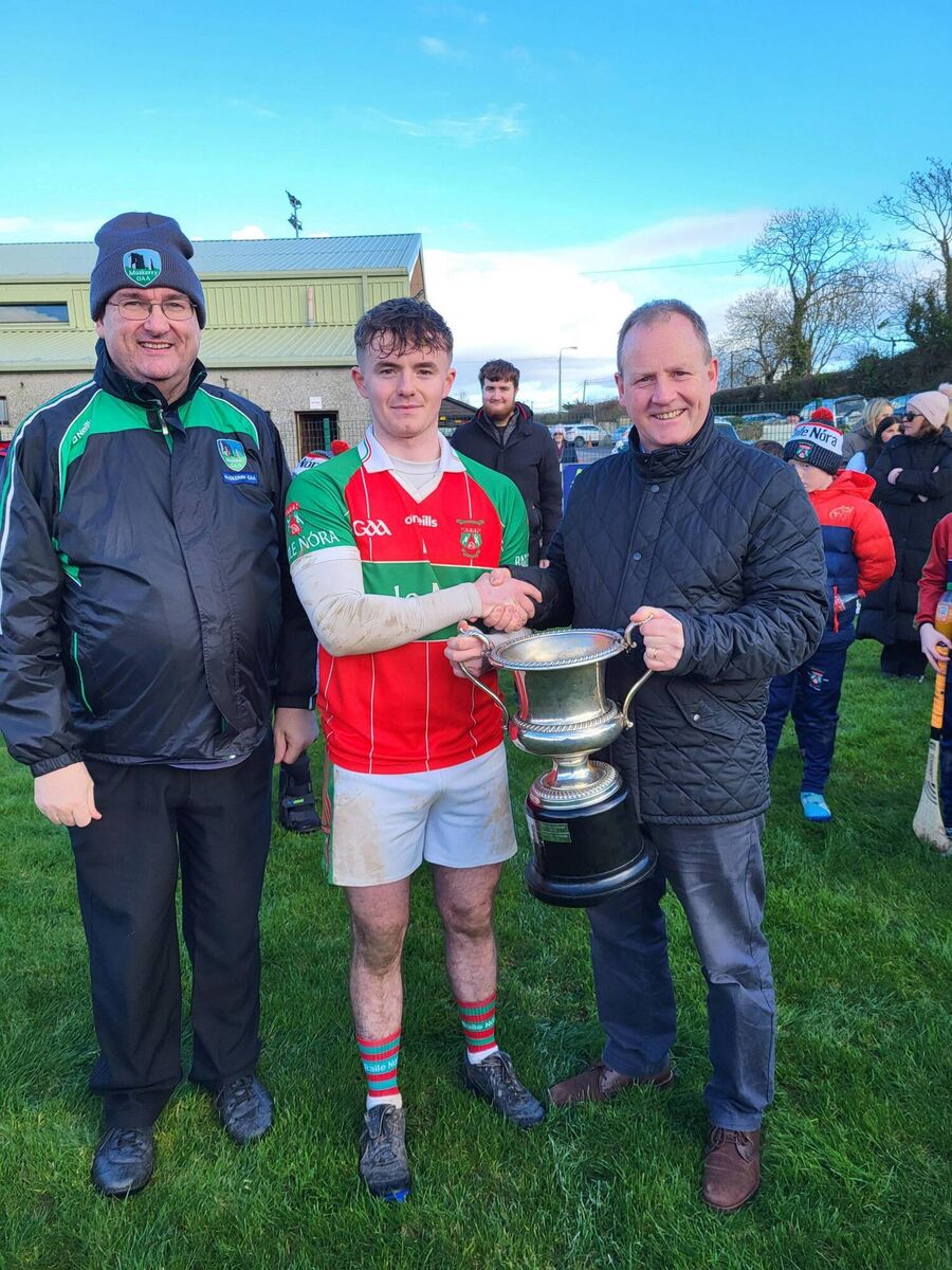 Ballinora captain Alex McAllen receives the Muskerry U21 A football championship trophy from Pat Barrett of Macroom Motors with Muskerry GAA chairman John Feeney also present.