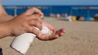 Woman hands applying sunscreen, with the beach in the background