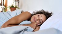 Young African American woman sleeping in modern bedroom with eyes closed.