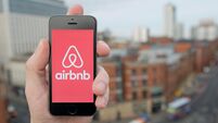 A man uses the Airbnb smartphone app while stood in a tall building overlooking a busy city street (Editorial use only)