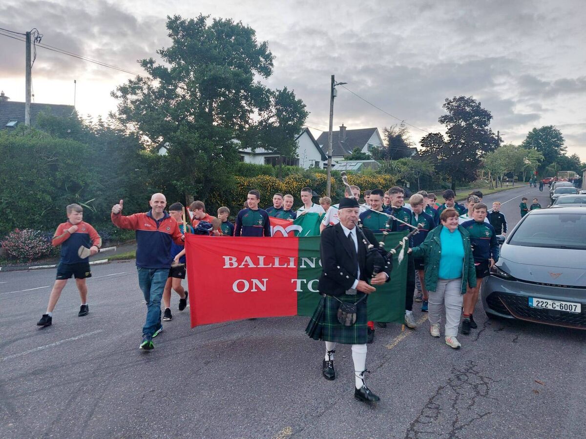 A lone piper leads the Ballinora Féile football team down at the homecoming.