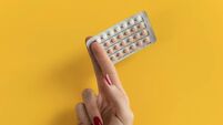 Female hand holding contraceptives against a yellow background.