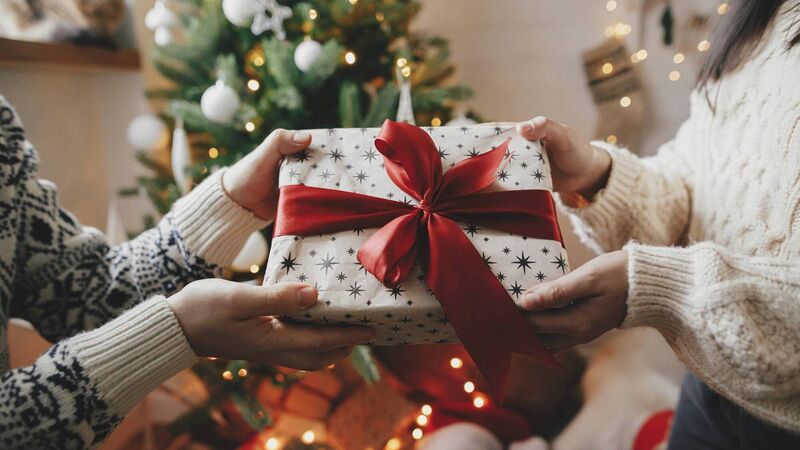 Couple exchanging christmas gift with red bow on background of christmas tree with lights. Stylish couple hands holding present