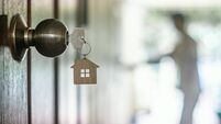 House key with home keyring in keyhole on wood door, copy space