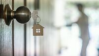 House key with home keyring in keyhole on wood door, copy space
